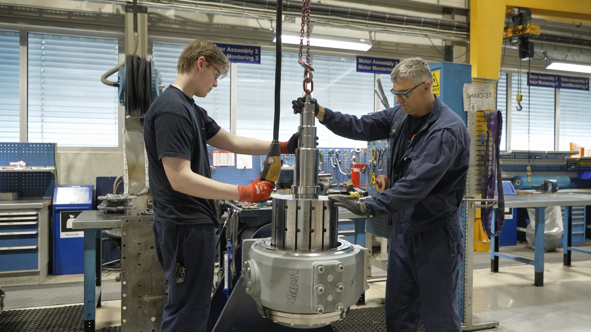 Apprentice and fitter lifting a motor part at the assembly station