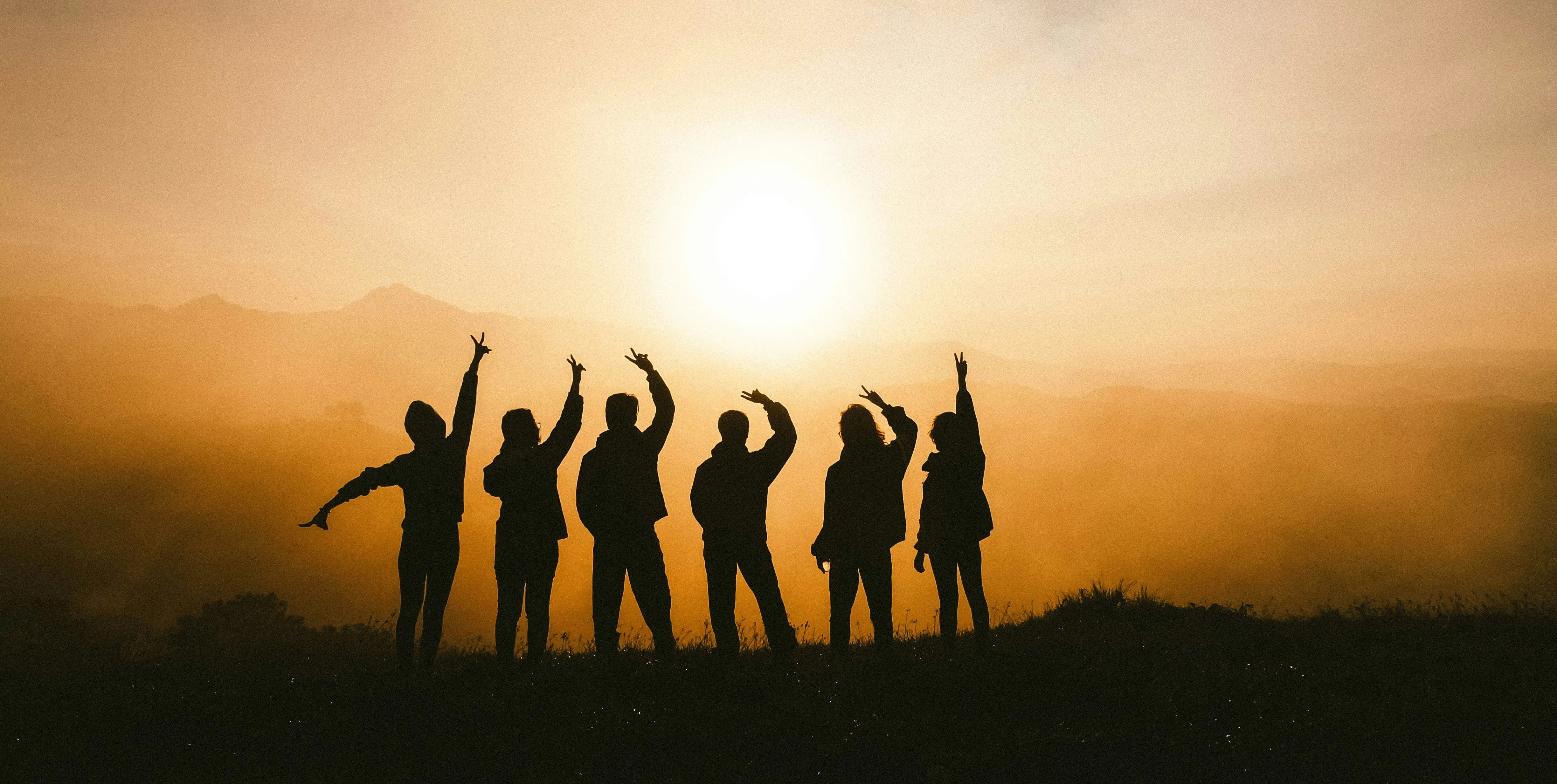 Silhouettes of people celebrating together on a hilltop at golden sunset