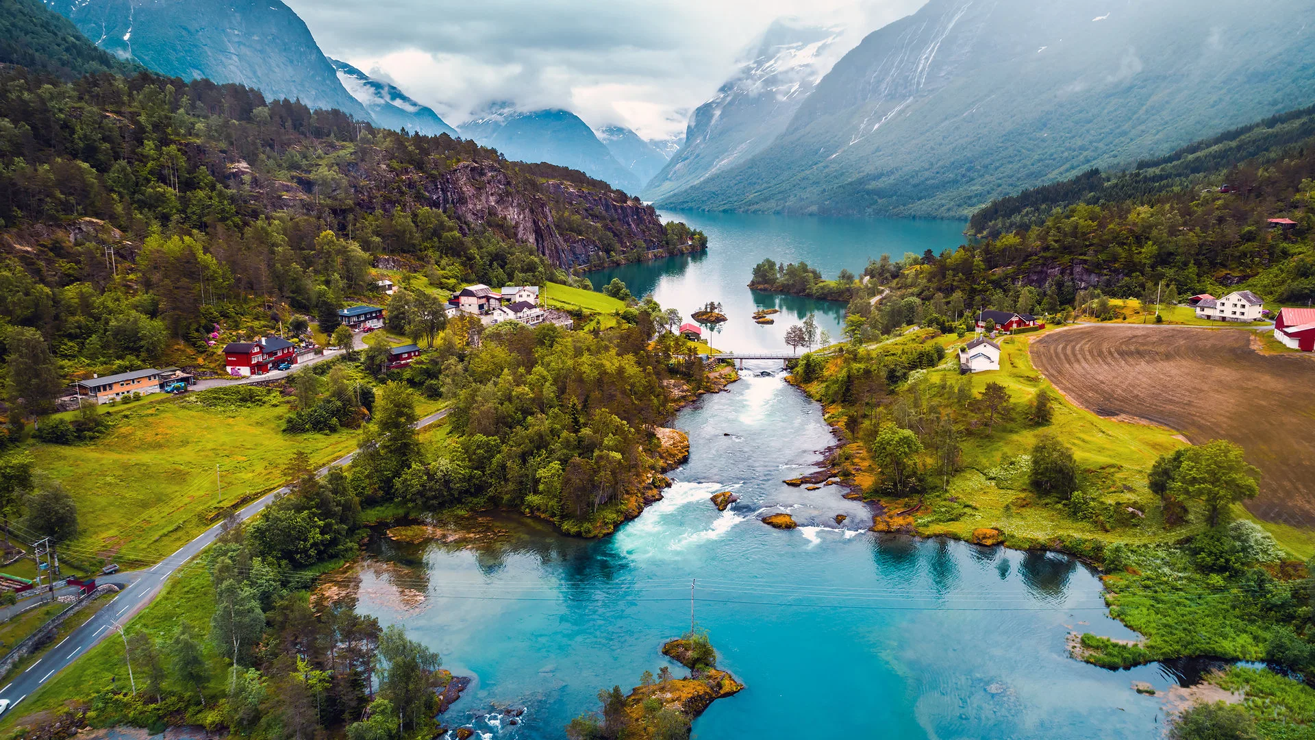 Dramatic Norwegian mountain landscape with green valleys, a winding river, and peaks shrouded in mist