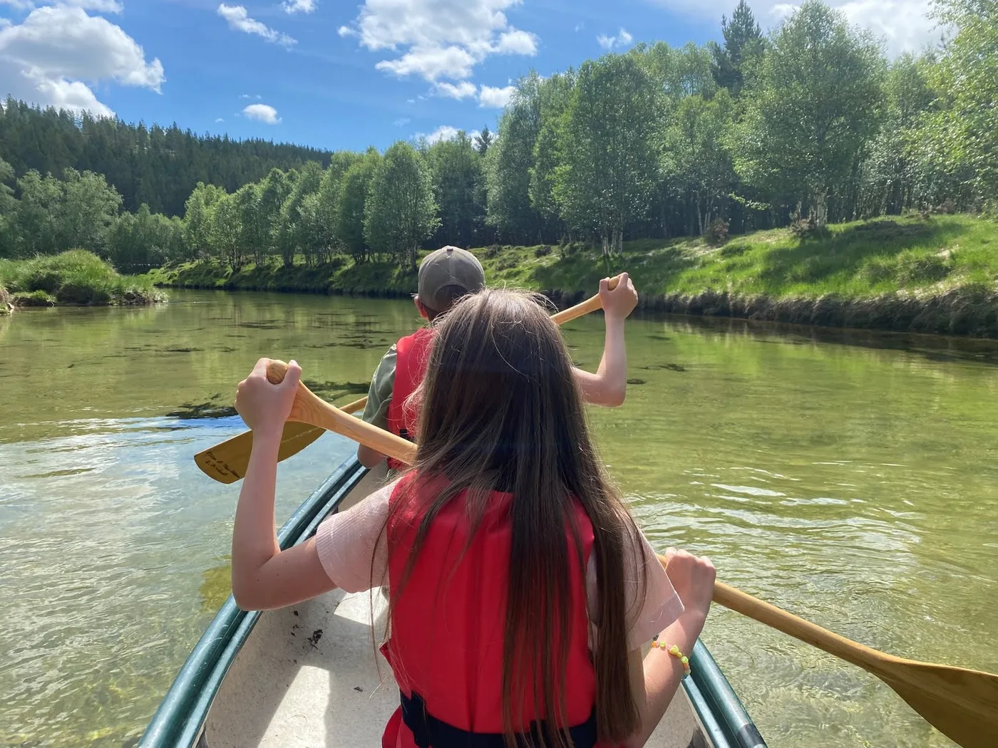 A man and a girl paddling a canoe on a calm river surrounded by lush green mountains in Folldal