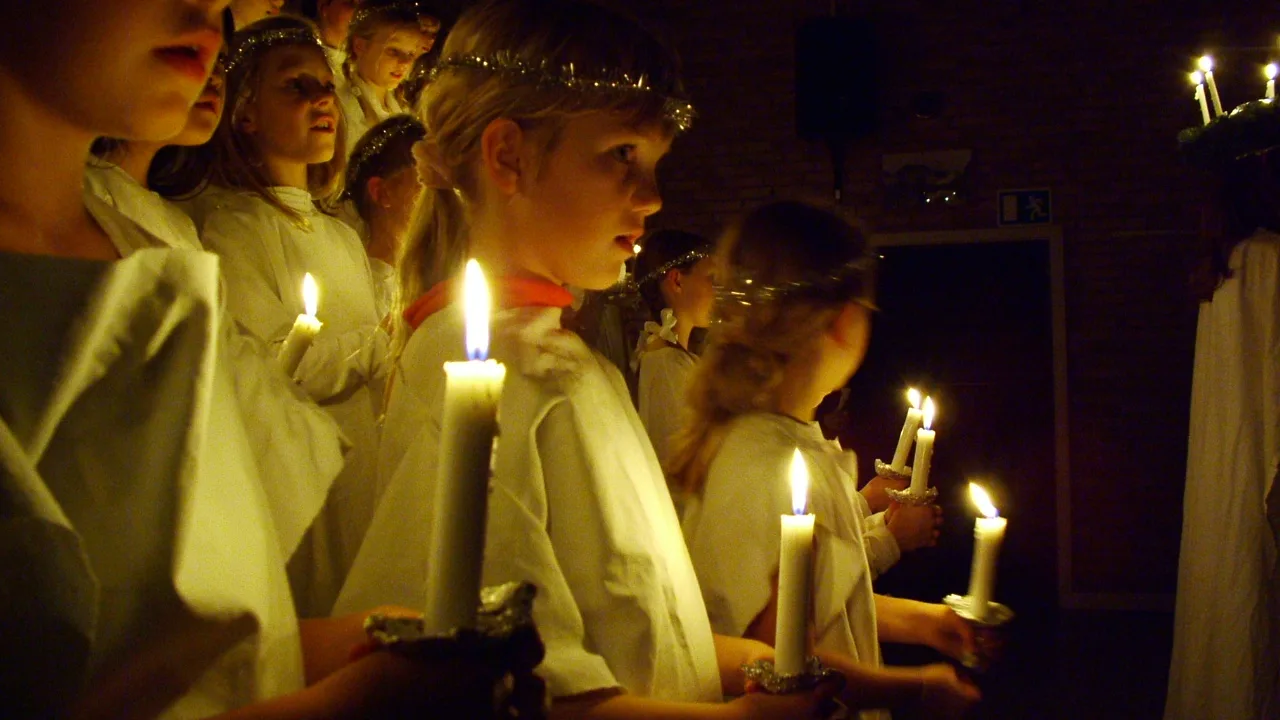 Children singing in a candlelit Lucia procession, dressed in white robes