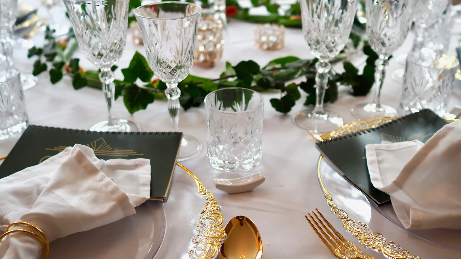 An elegantly set table at Oldemors Hus with gold-plated cutlery, crystal glasses, and white tablecloth
