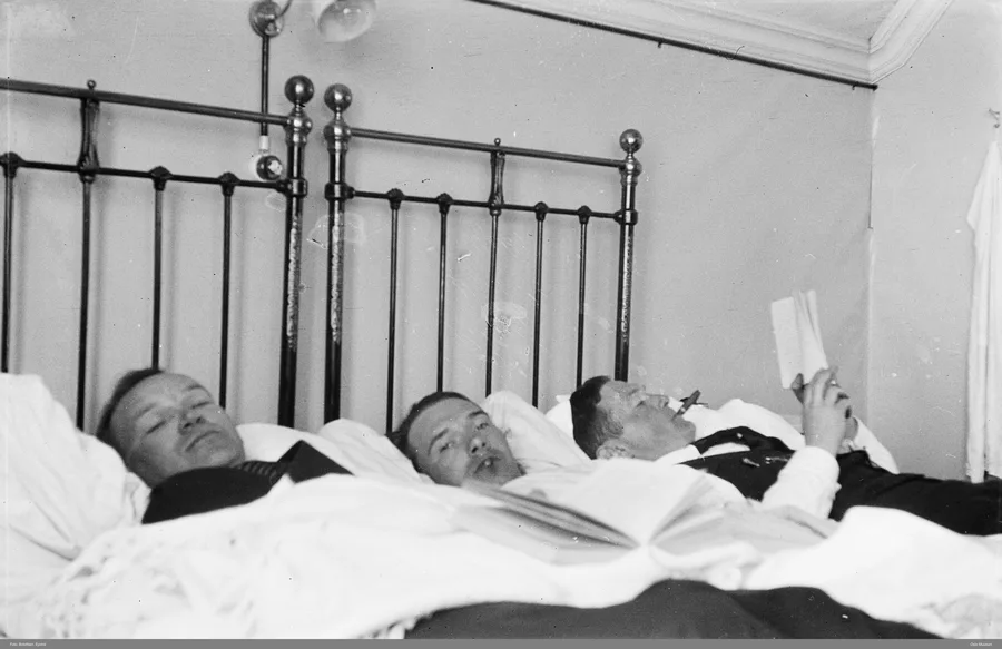 Three men lying in bed reading books during an Easter vacation in Dombås, black and white photograph from the early twentieth century