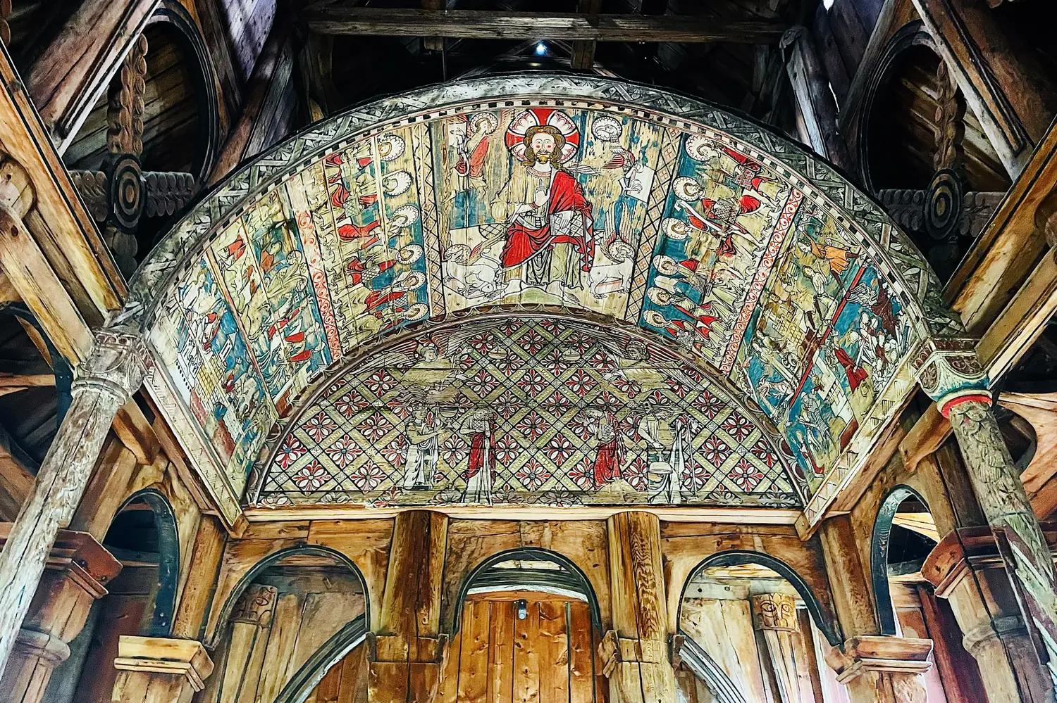 The painted baldachin inside Torpo Stave Church showing a rosy-cheeked Christ enthroned among the apostles under a curved barrel vault