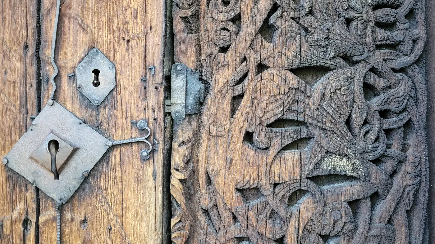 Close-up of an iron lock plate and key-hole shield on the doorway of Torpo Stave Church, set against deep dragon-style carvings