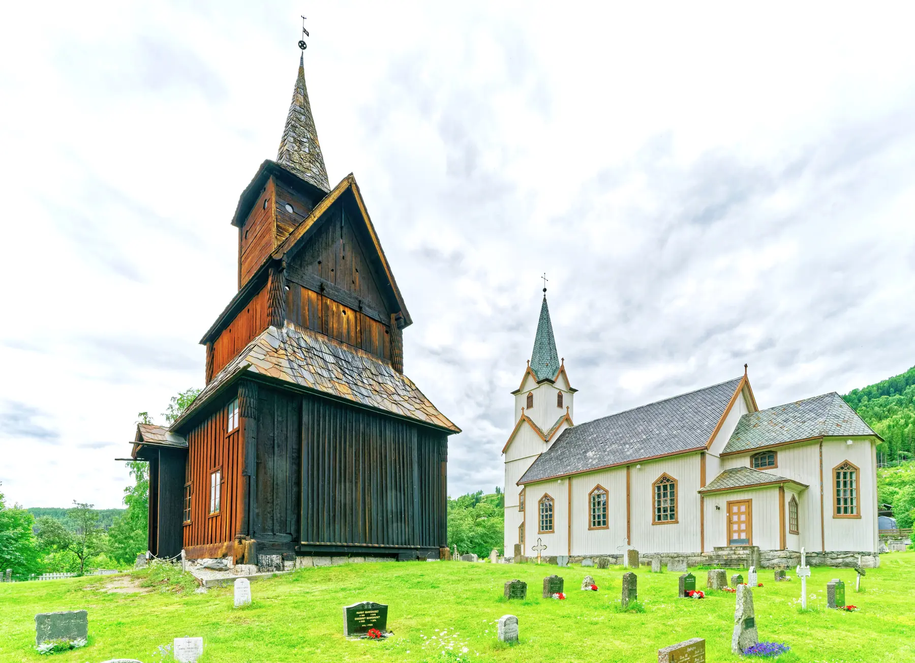 Torpo Stave Church and the 1880 white parish church standing side by side in summer, separated by only metres of churchyard
