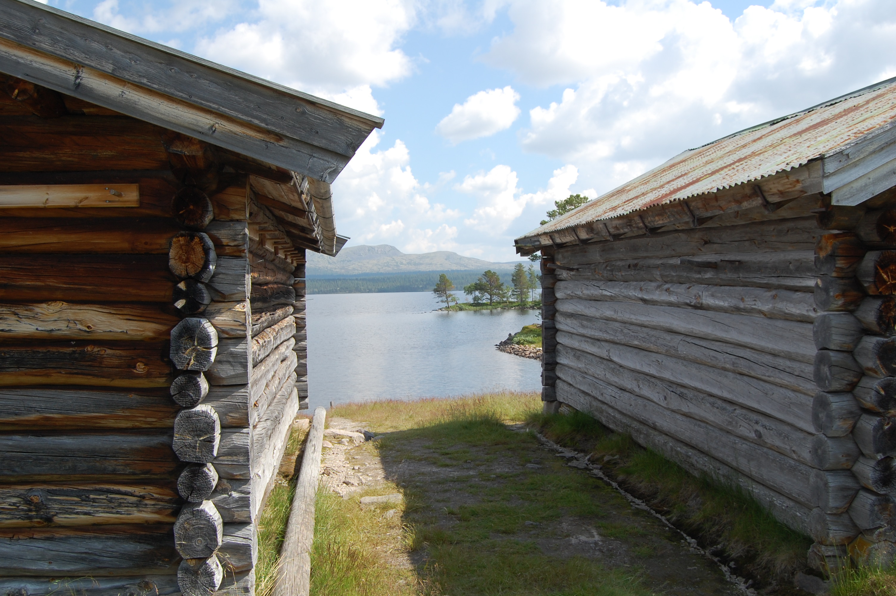 A cluster of Fiskevollen log buildings — grass-roofed cabins and lower naust along the lakeshore