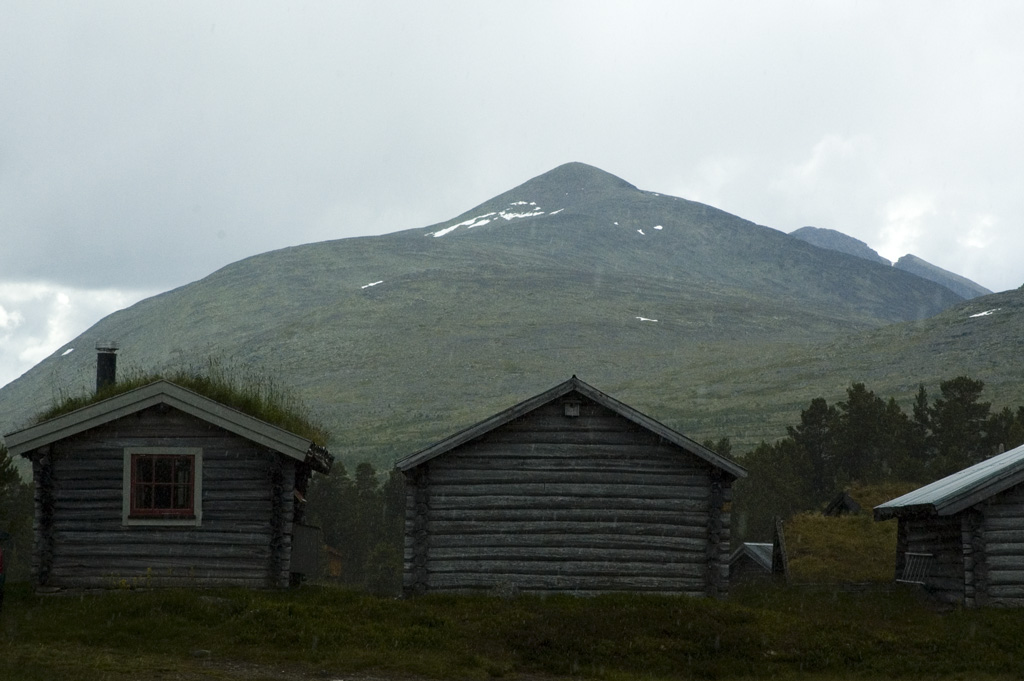 Sod-roofed log buildings at Fiskevollen with Sølenfjellet rising in the background under cloud
