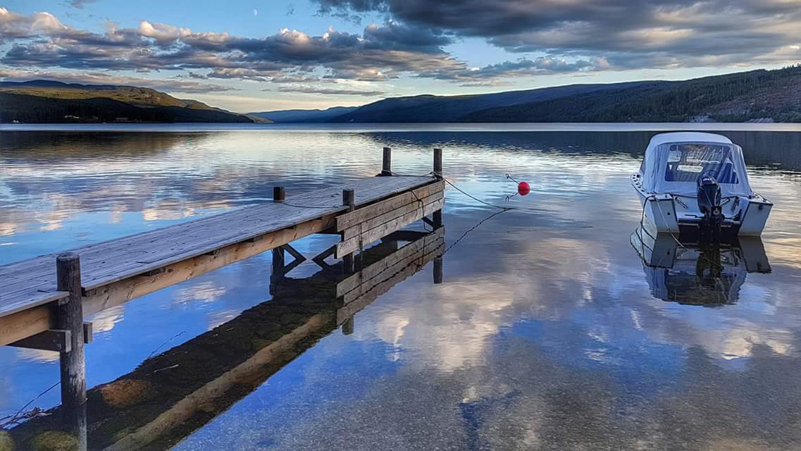 A wooden dock at sunset on Storsjøen, with a small boat moored alongside