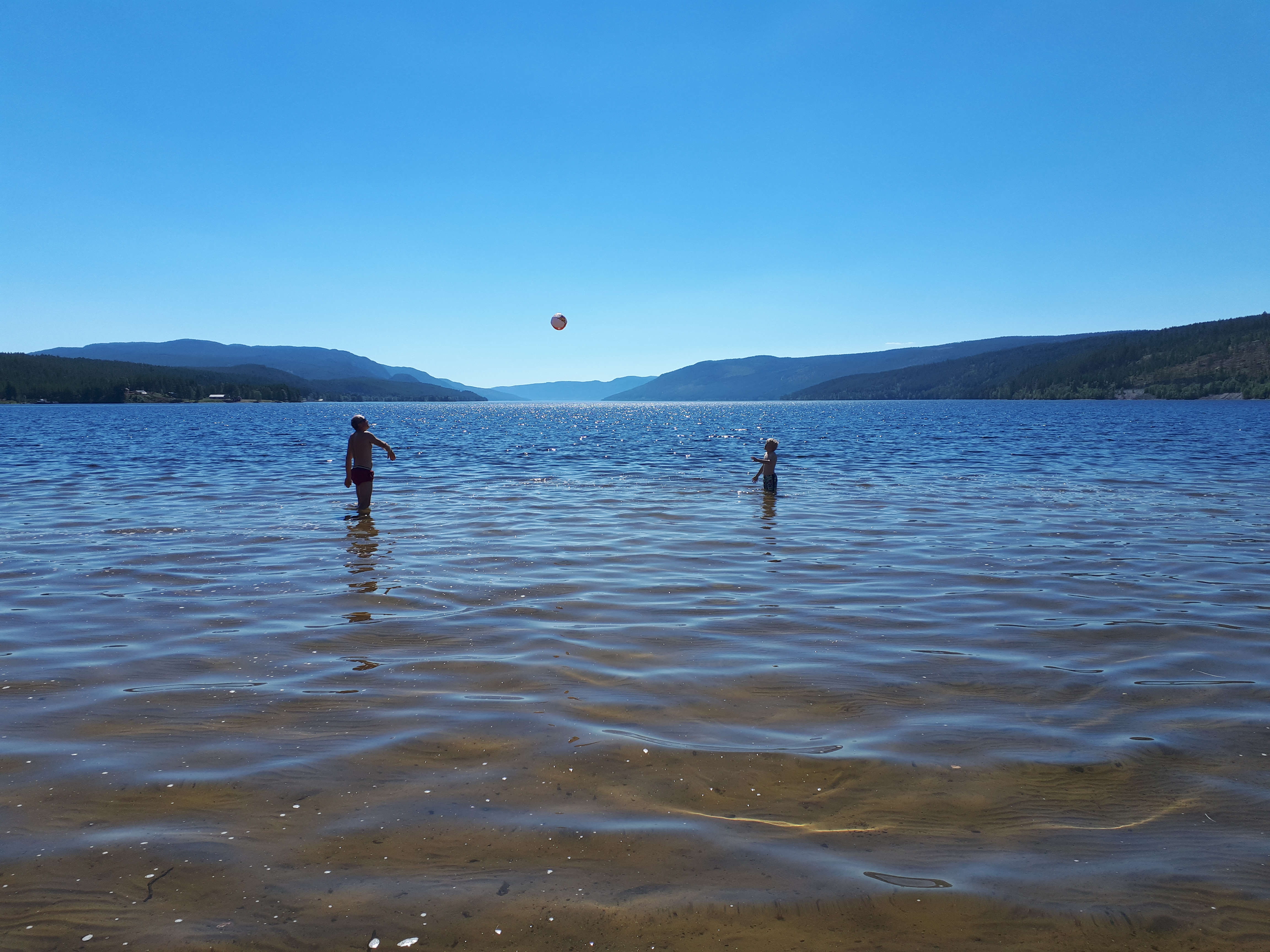 Two children playing in the water at the Sanaodden beach on Storsjøen, mountains in the distance