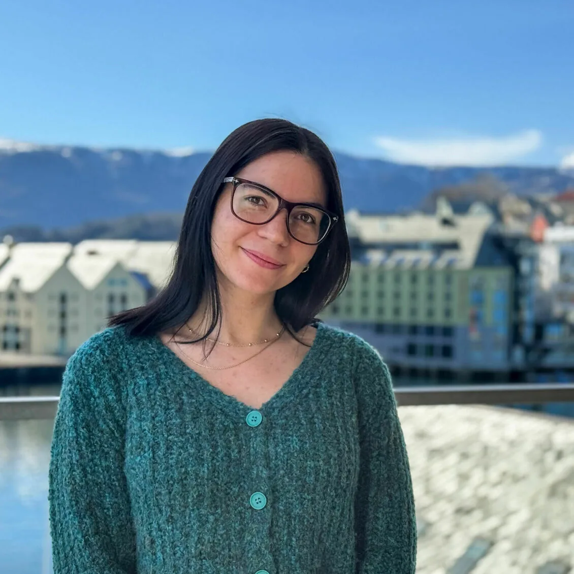 Portrait of Gema Baldo Llorca smiling in a green cardigan with the Ålesund waterfront and mountains behind her.
