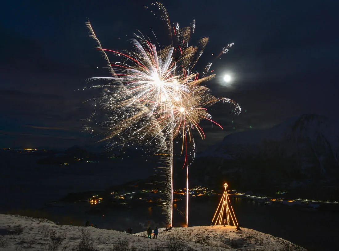 Large firework lighting up the night sky above the coastal village of Brattvåg, with a lit Christmas tree and lights along the fjord