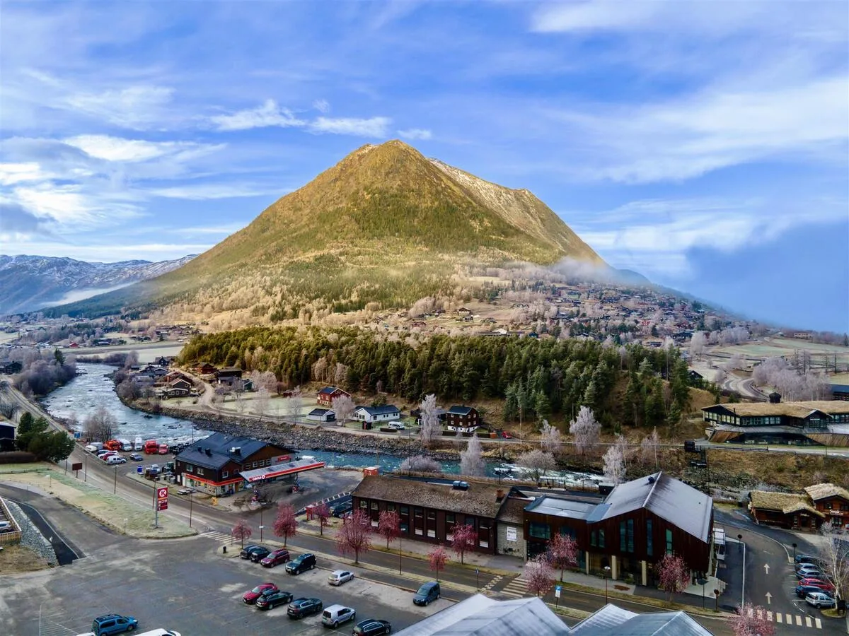 Aerial view of Lom village showing the river Bøvra, traditional wooden buildings, and the towering Lomseggen mountain behind