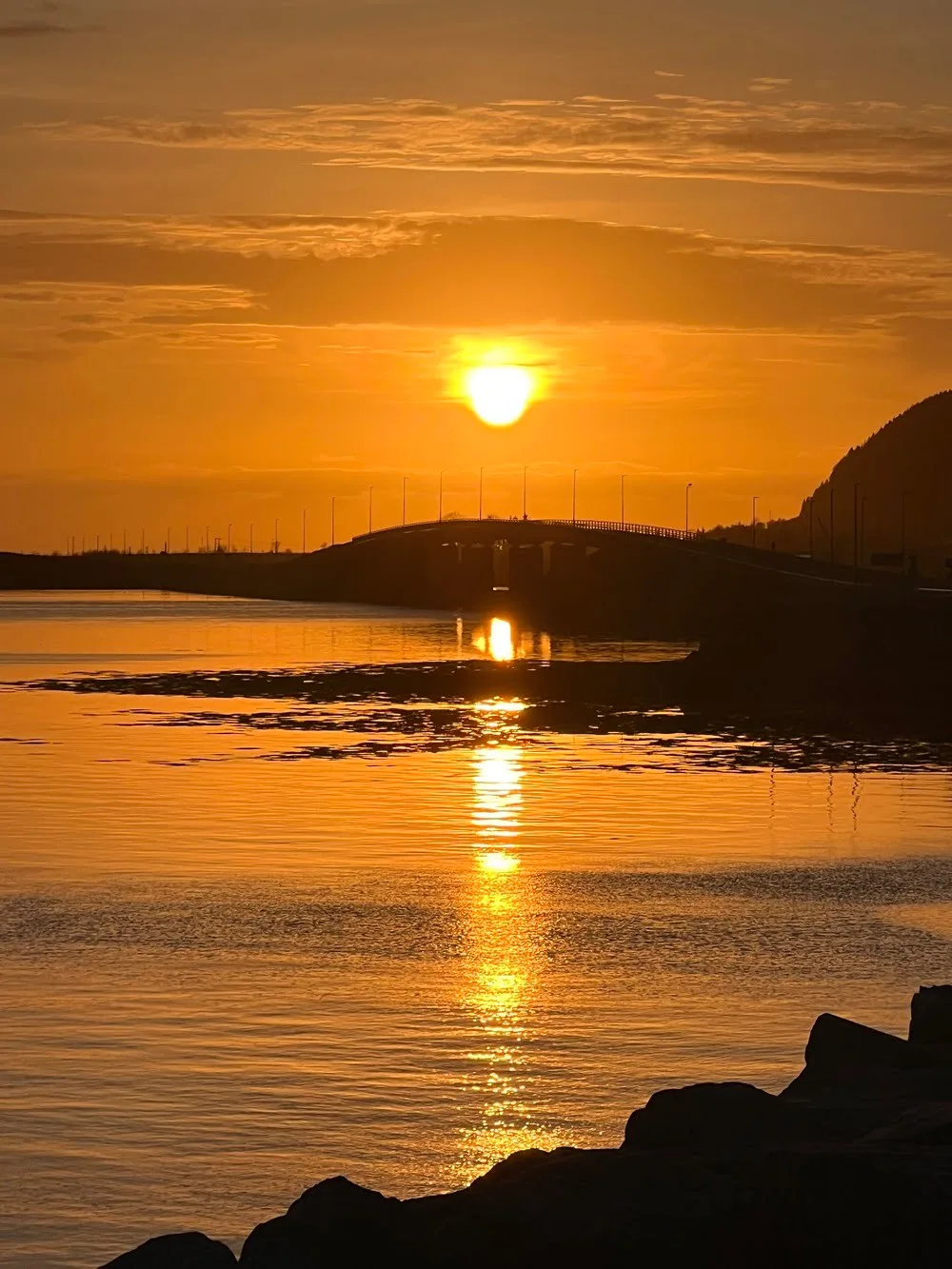 A bright orange sunset over calm fjord waters in Søvik