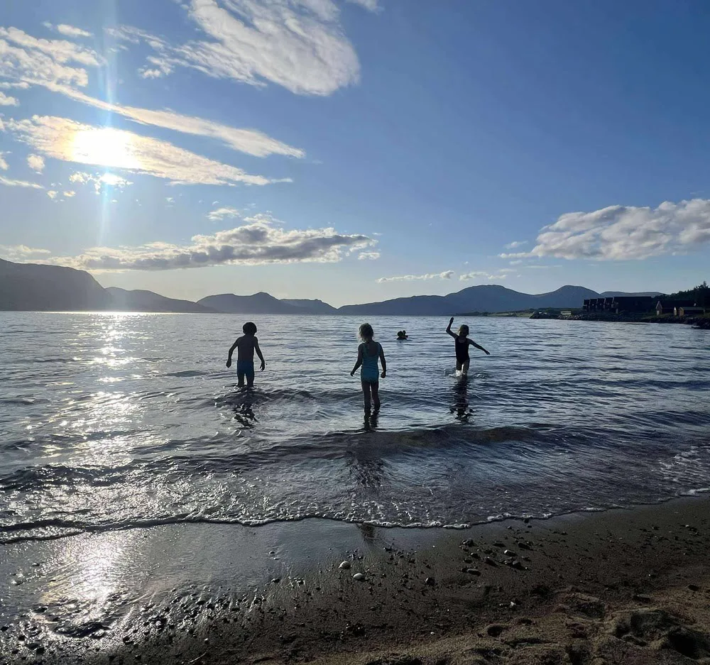 Children playing in the shallow water on a sandy beach in Tomrefjord on a sunny day, with mountains in the background